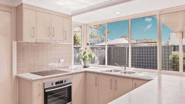 Una cocina moderna con armarios color beige, horno empotrado, pileta doble y ventana con vista al jardín trasero.