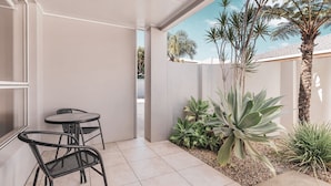 Un patio con dos sillas de metal negro y una mesa, rodeado de diversas plantas y una palmera.