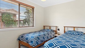 Ein Schlafzimmer mit zwei Einzelbetten, einem Nachttisch, einer Lampe und einem Fenster mit Jalousien.