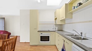 Eine kleine Küche mit Einbauofen, Mikrowelle und Spüle. Ein Holztisch mit Stühlen und eine Tür mit einer Nummer sind sichtbar.