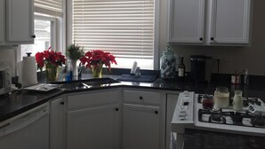 Una cocina con armarios blancos, estufa, lavamanos y ventana con persianas.
