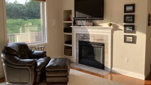 Una sala de estar con chimenea, un sofá de cuero, un reposapiés, un televisor montado sobre la chimenea y cuadros enmarcados en la pared.