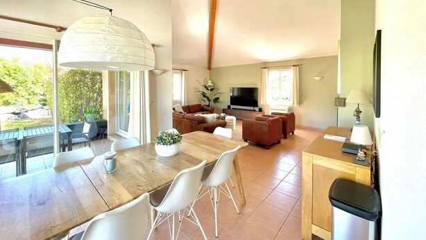A spacious living area with a dining table, chairs, sofas, a TV, and a large window overlooking greenery. - Villa du Bonheur for 8 people with private pool (Vallon-Pont-d'Arc)