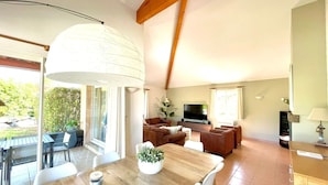 A spacious living area with a wooden dining table, a sofa set, a TV, and a large window. - Villa du Bonheur for 8 people with private pool (Vallon-Pont-d'Arc)
