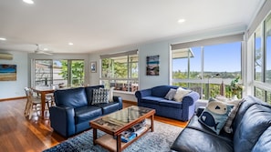 A spacious living room with a dining area, large windows, and a balcony with a view.