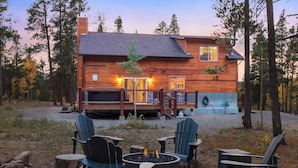 A cabin with a deck, a fire pit, and Adirondack chairs.