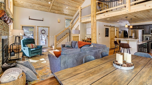 A spacious living area with a wooden ceiling, a blue sofa, a dining table with candles, and a kitchen in the background.