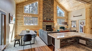 A log cabin interior with a stone fireplace, wooden walls, and large windows.