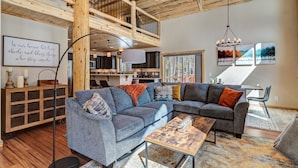A spacious living room with a large sectional sofa, a wooden ceiling, and a view of the kitchen.