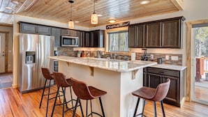 A modern kitchen with a large island, stainless steel appliances, dark wood cabinets, and a wooden ceiling.