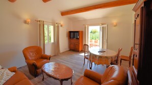 Amplia sala de estar con vigas de madera, mobiliario de cuero, una televisión y un comedor con mesa y sillas.