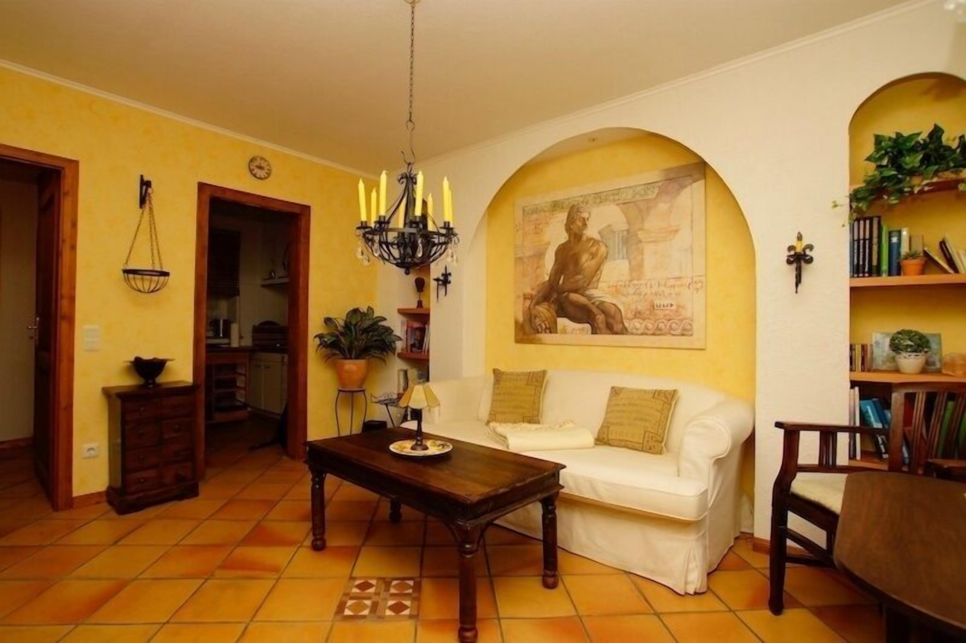 Uma sala de estar com sofá branco, mesa de centro de madeira, lustre e um quadro na parede.