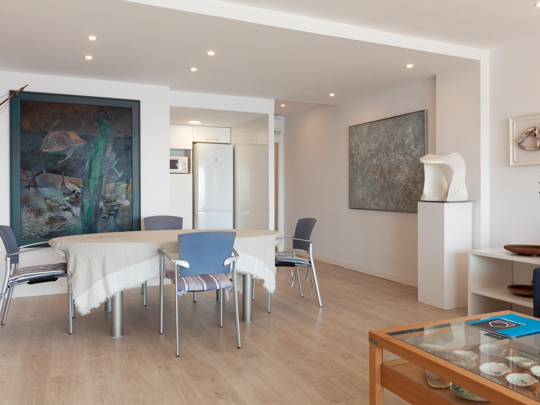 Un comedor moderno con una mesa, sillas y una mesita de centro de cristal decorada con objetos decorativos.