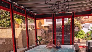 An indoor swimming pool with clear water, surrounded by a red and black structure, and a stone wall in the background.