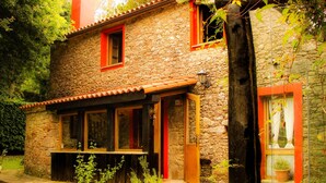 A stone house with a tiled roof, wooden shutters, and a small porch with a bench.