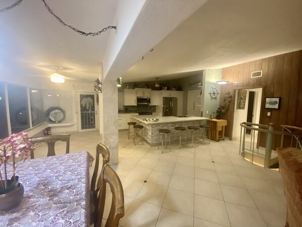 A spacious kitchen with a central island, bar stools, and a dining area with a table and chairs. - Water Front 3/3 Family and Boat Friendly Home, Great Views (Islamorada)