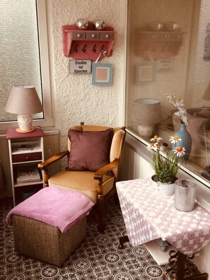 A cozy room with a chair, a small table with a vase, and a shelf with decorative items. - Fewo Schimmer & Wurmbergblick & Uden (Braunlage)