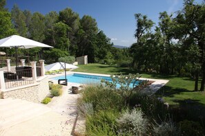 Un jardín trasero con piscina, un patio con mobiliario exterior y un muro de piedra.