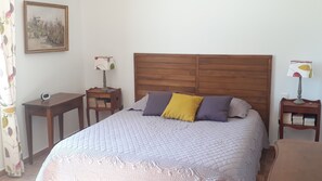 Un dormitorio con cabecera de madera, cama con cubrecama acolchado, dos mesitas de noche con lámparas y un cuadro en la pared.