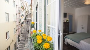 Una calle estrecha flanqueada por edificios, una escalera que asciende y un balcón con flores amarillas.