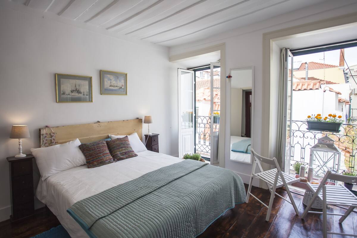A bedroom with a bed, a nightstand, two framed pictures, and a view of the outside balcony.