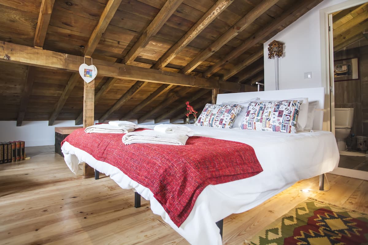A bedroom with a wooden ceiling, a white bed with patterned pillows, and a red blanket.