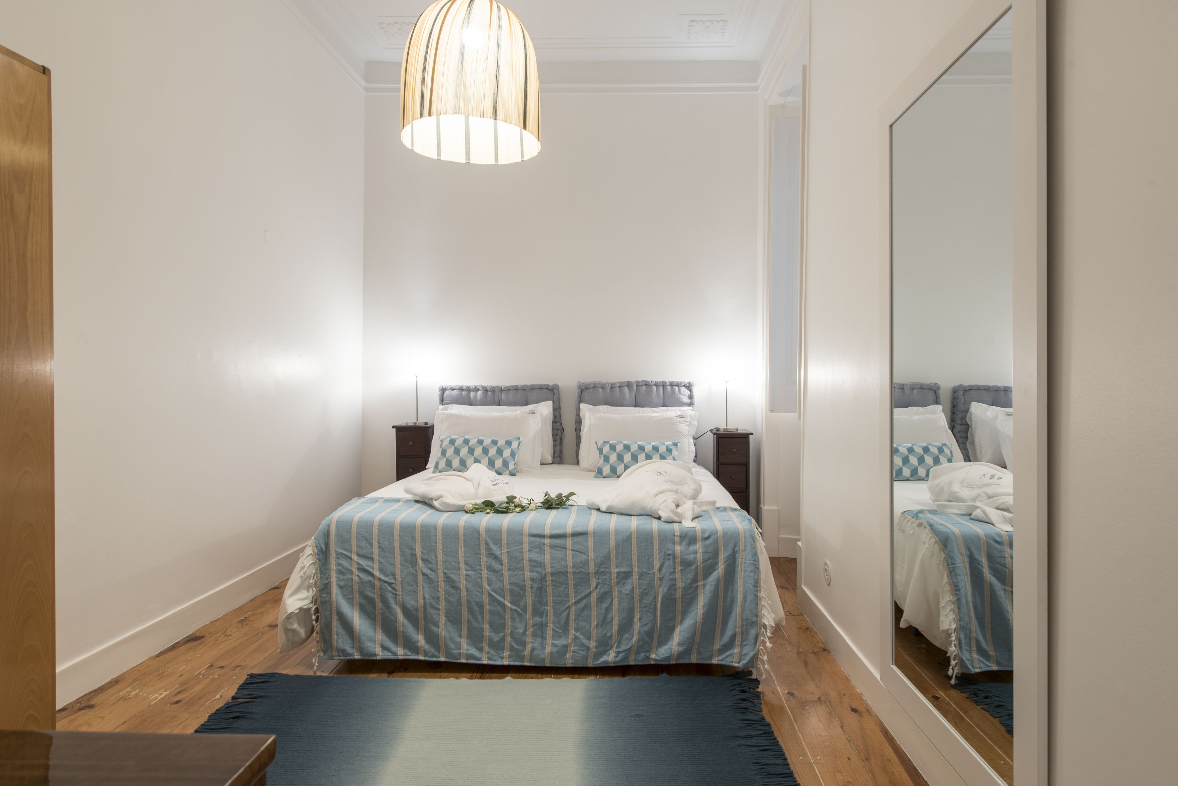 Un dormitorio con cama, mesitas de noche, un espejo y una lámpara colgante.