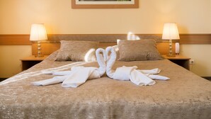 A neatly made bed with towels arranged in a swan shape, two bedside lamps, and a framed picture on the wall. - Aquasol Resort (Mosonmagyarovar)