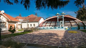 A courtyard with a brick pathway, a covered seating area, and a building with a red roof. - Aquasol Resort (Mosonmagyarovar)