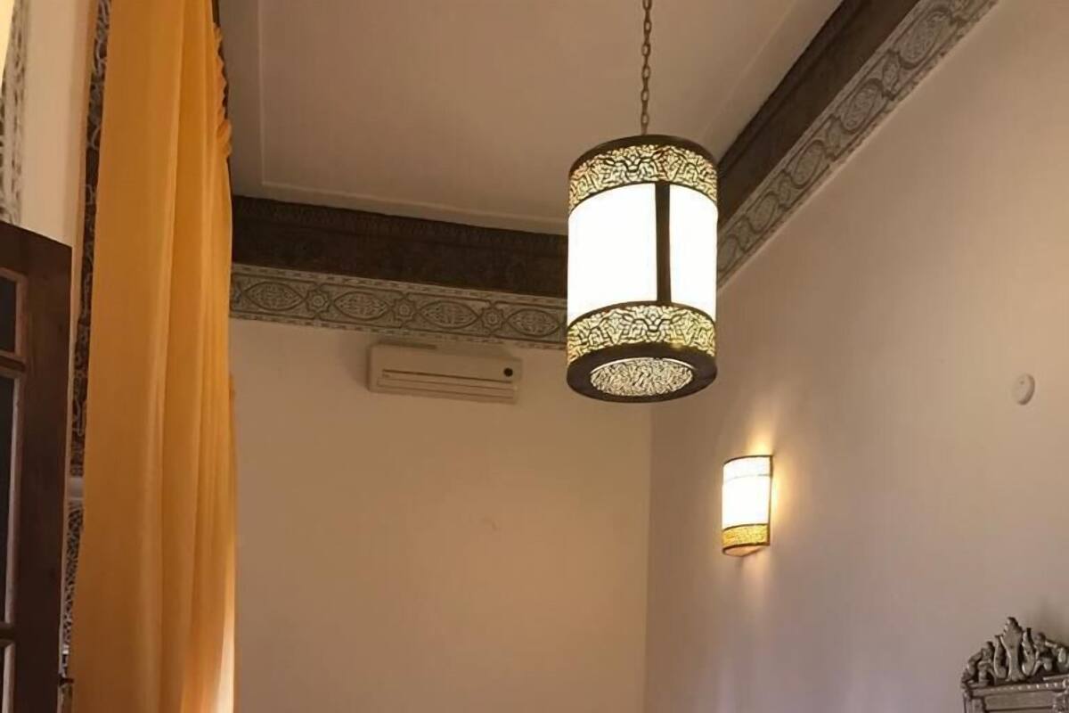 A hotel room with a bed, a sofa, a table, a hanging light fixture, and a wall-mounted lamp.