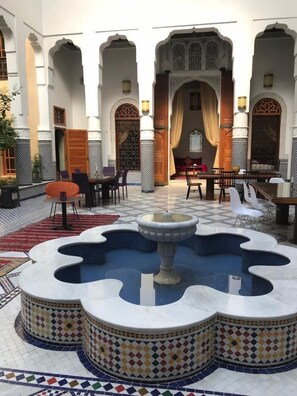 Um pátio com uma fonte central, áreas de estar e arquitetura tradicional marroquina.