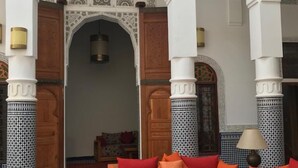 A lounge area with a red sofa set, teal armchairs, and a glass coffee table. - Riad Jasmins & Spa (Fes)