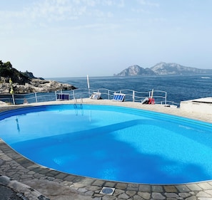 A clear blue pool with lounge chairs and a view of the sea and mountains.
