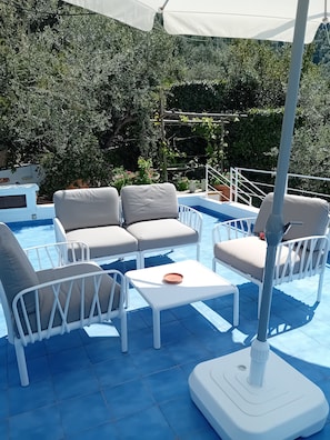 Ein Poolbereich mit weißen Liegestühlen und einem Tisch, umgeben von einem blau gefliesten Boden.