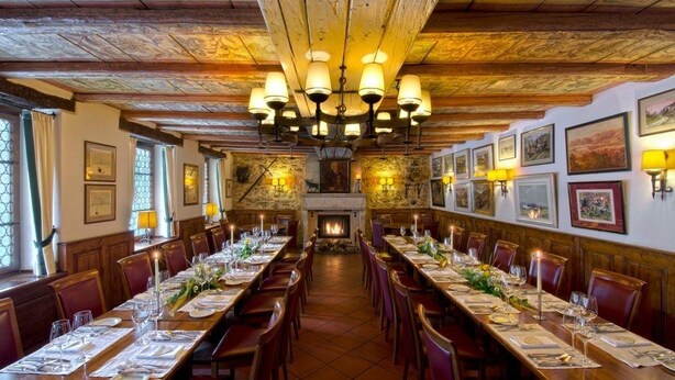 Een lange eettafel gedekt voor een maaltijd in een kamer met houten balken en een open haard.