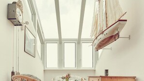 Een ruime kamer met een hoge plafond, grote ramen, een houten kast en rieten meubels.