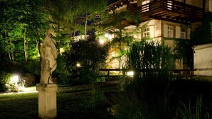 Een traditioneel Japans gebouw met een houten balkon, omringd door weelderige begroeiing en een stenen standbeeld op de voorgrond.
