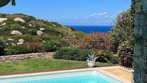 A pool with clear blue water, surrounded by a stone wall and a view of the ocean and hills. - Villa “Le Terrazze” (Lumio)