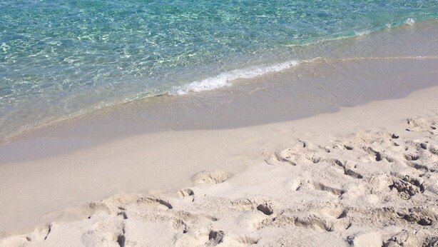 A beach with clear turquoise water, sandy shore, and footprints in the sand. - Villa “Le Terrazze” (Lumio)