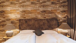 Ein Bett mit Steinwand im Hintergrund, zwei Nachttischlampen und ein dunkles Kopfteil.