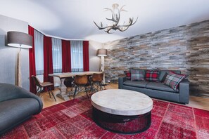 A modern living room with a stone wall, a round coffee table, a sofa with plaid cushions, a dining table with chairs, and a chandelier.