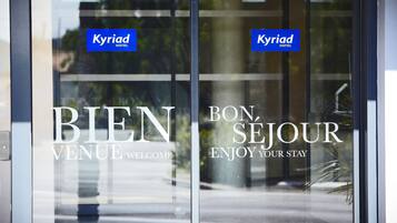 L’entrée d’un hôtel, avec une enseigne « Kyriad Hotel » et des messages d’accueil bilingues.