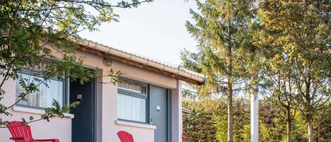 Un edificio moderno con techo plano, dos sillas Adirondack rojas y una pequeña mesa con un vaso de agua.