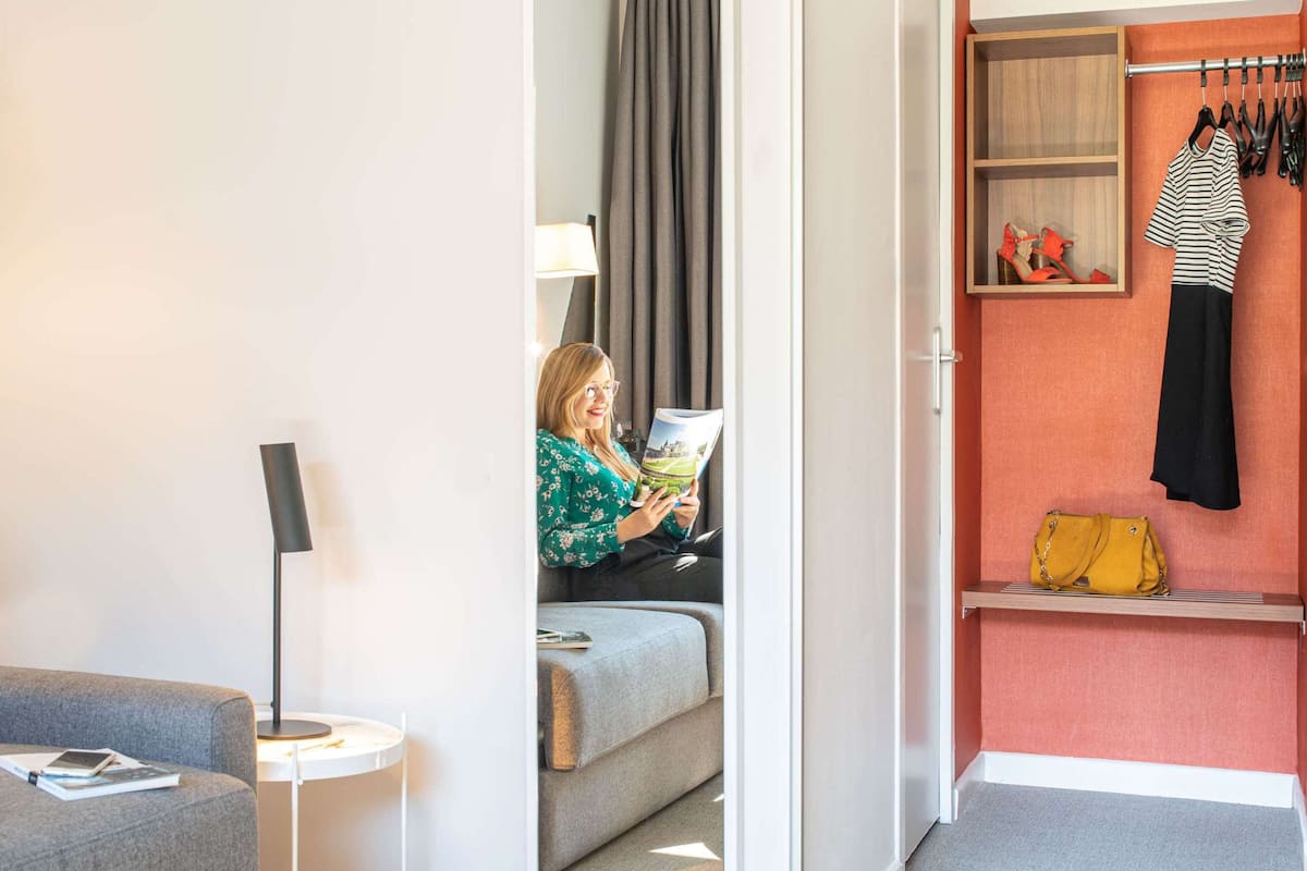 Une pièce comprenant un canapé, un coin lecture, une lampe, un porte-chaussures et une petite étagère sur laquelle se trouve un sac à main.
