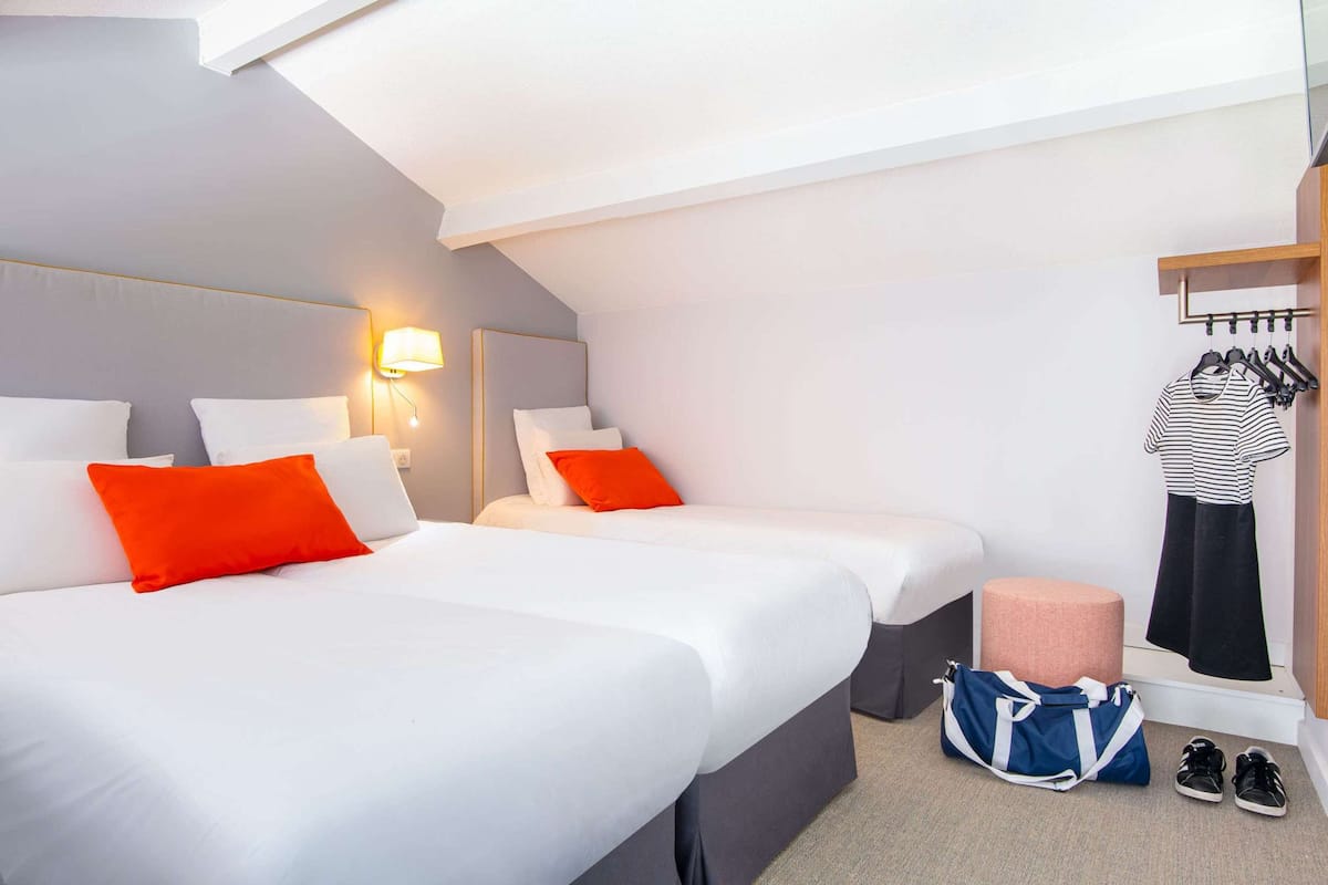 Une chambre d’hôtel avec deux lits, une table de chevet, une lampe, une armoire et une valise.