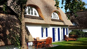 Een traditioneel huis met rieten dak, een eetgedeelte met houten meubels en een verzorgd gazon.