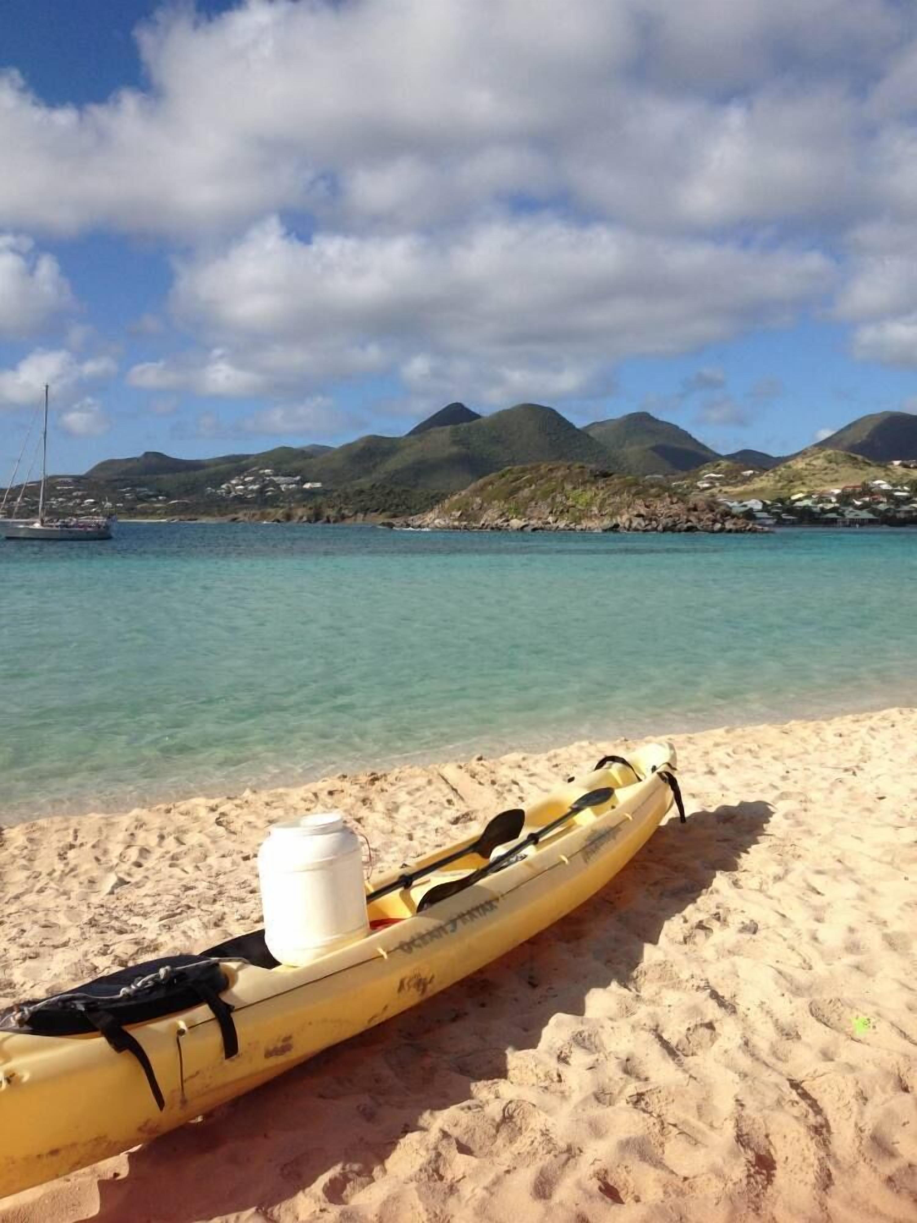 A kayak on a sandy beach with a clear view of the sea and mountains in the background.