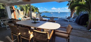 Un área de comedor al aire libre con vistas al mar, sillas de mimbre, una mesa y una terraza de madera.