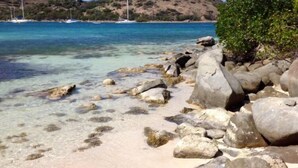 A beach with clear turquoise water, large rocks, and a sailboat in the distance. - Waterfront villa 4 bedrooms, 3 bathrooms with pool, kayaks, high speed wifi (Cul-de-Sac)