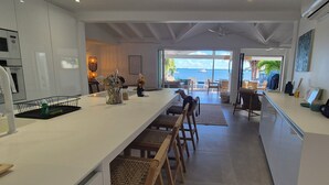 A modern kitchen with a long counter, white cabinets, and a view of the sea through large windows. - Waterfront villa 4 bedrooms, 3 bathrooms with pool, kayaks, high speed wifi (Cul-de-Sac)